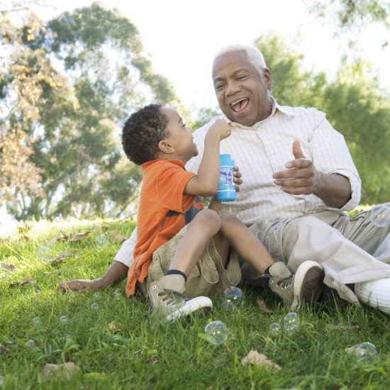 Older man and young child blowing bubbles in a field