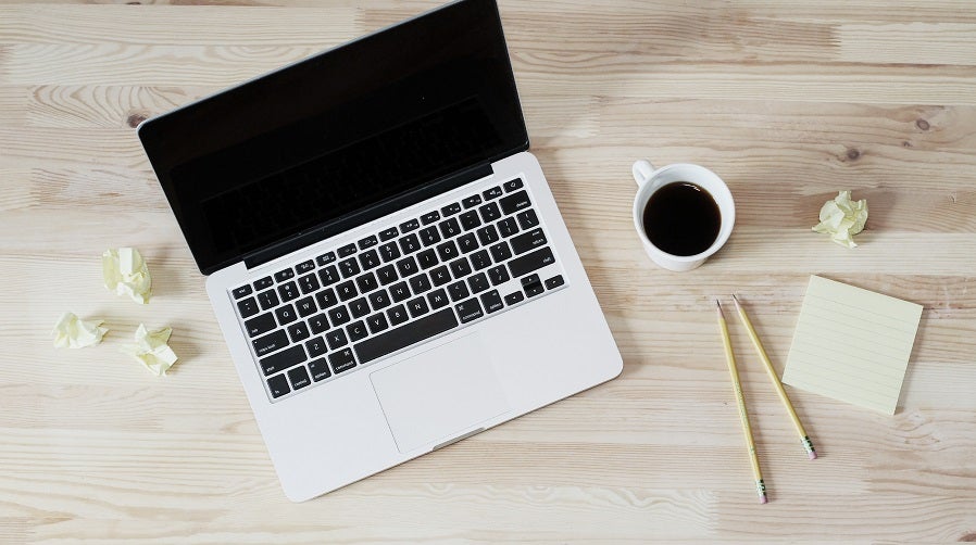 An open laptop computer, a cup of coffee, pencils, and paper