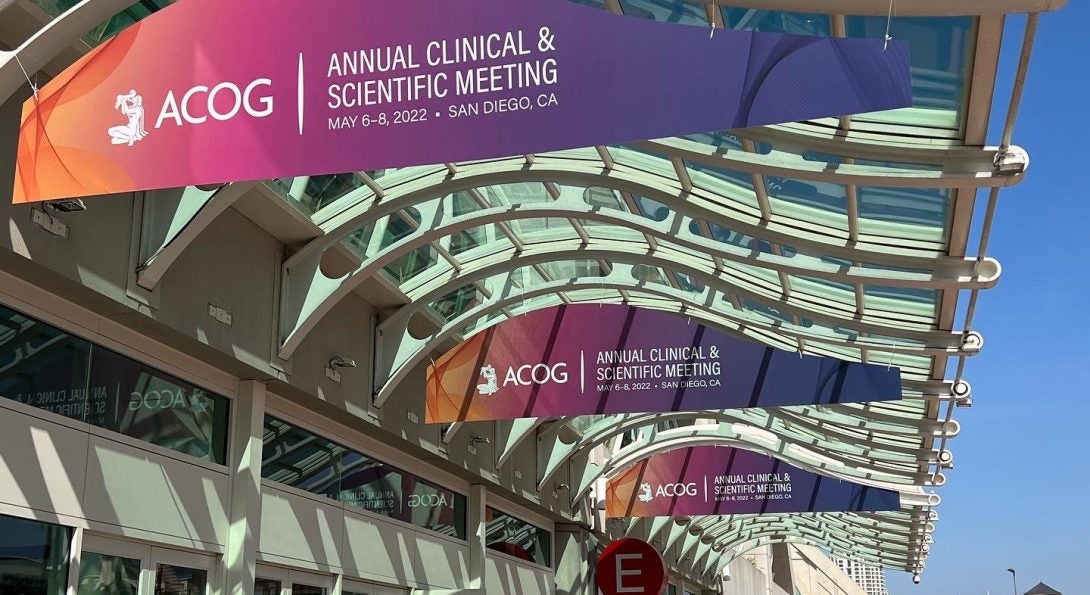 Three orange, pink, and purple gradient signs that says Annual Clinical & Scientific Meeting that are hanging overhead outside