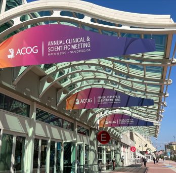 Three orange, pink, and purple gradient signs that says Annual Clinical & Scientific Meeting that are hanging overhead outside
                  