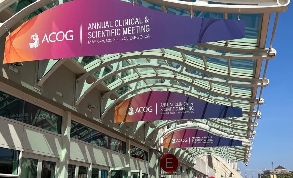 Three orange, pink, and purple gradient signs that says Annual Clinical & Scientific Meeting that are hanging overhead outside